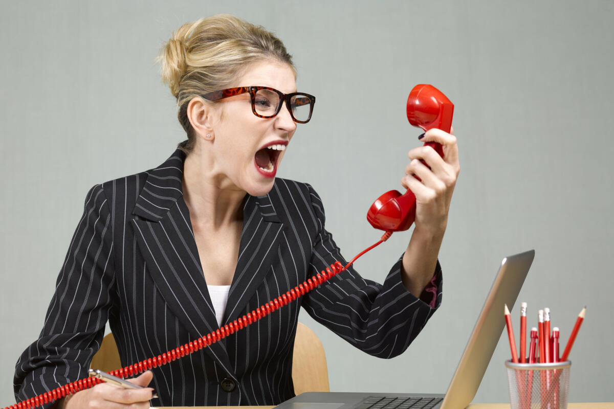 Wütenden Businessfrau sitzt an ihrem Schreibtisch und schreit in das Telefon © Peter Dazeley / Getty Images