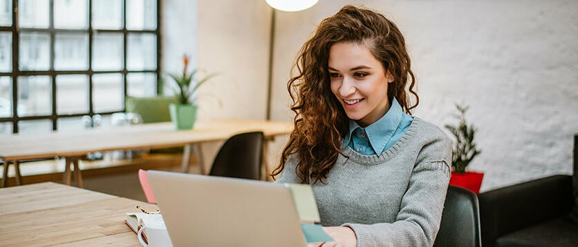 Junge Frau sitzt lächelnd vor Laptop © nortonrsx / Getty Images