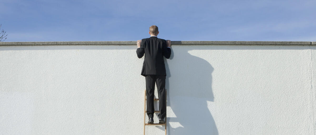 Geschäftsmann auf Leiter mit Blick über die Mauer  © Johnny Valley / Getty Images
