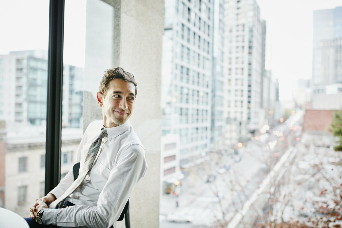 Geschäftsmann im Büro sitzend mit Blick auf die Stadt © Thomas Barwick / Getty Images