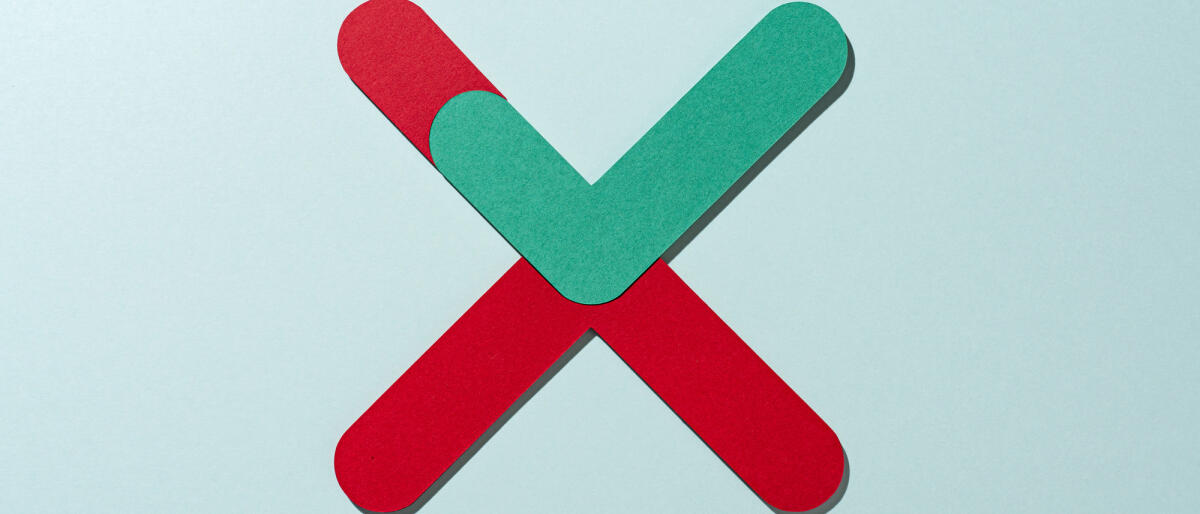 Papierhandwerk Grün gefärbtes Häkchen eingebettet in rot gefärbtes Kreuzzeichen auf grünem Hintergrund direkt über der Ansicht © MirageC / Getty Images