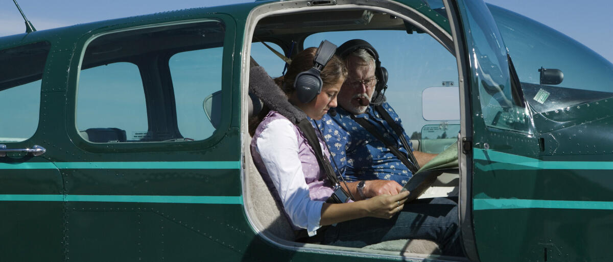 Teenager-Mädchen und Fluglehrer mit Blick auf die Karte im Flugzeug © Karen Moskowitz / Getty Images