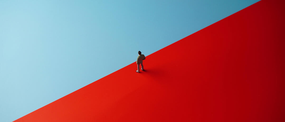 Illustration eines Geschäftsmanns, der auf einer roten Fläche steht und überlegt auf die blaue zu gehen © Wong Yu Liang / Getty Images