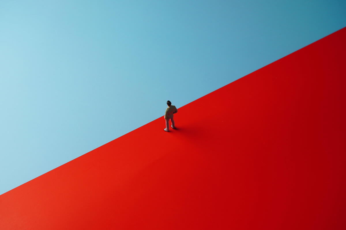 Illustration eines Geschäftsmanns, der auf einer roten Fläche steht und überlegt auf die blaue zu gehen © Wong Yu Liang / Getty Images