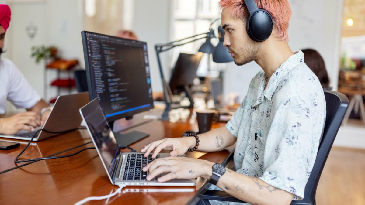 Junger Mann mit Kopfhörern bei der Arbeit am Computer in einem Startup-Büro © Luis Alvarez / Getty Images