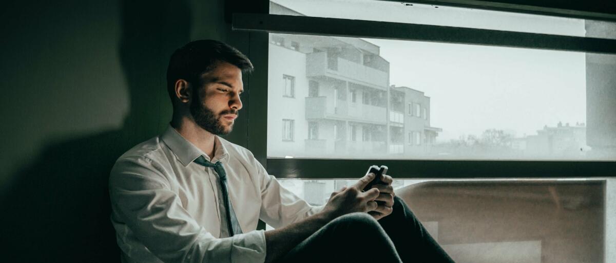 Ein Mann offensichtlich unglücklich sitzt auf dem Boden und hat sein Handy in der Hand  © Borna Hržina / Unsplash