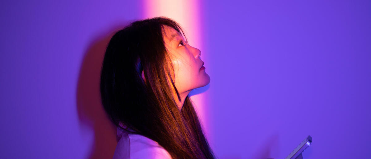 Asiatische junge Frau benutzt ihr Smartphone, während sie nachts im Scheinwerferlicht steht © Qi Yang / Getty Images