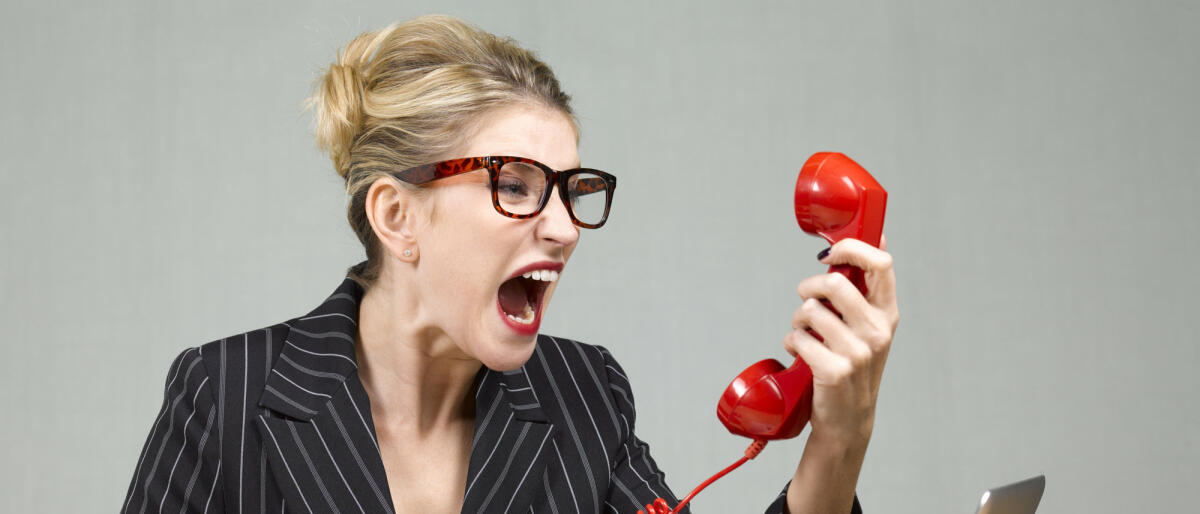Wütenden Businessfrau sitzt an ihrem Schreibtisch und schreit in das Telefon © Peter Dazeley / Getty Images