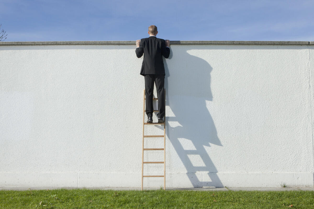 Geschäftsmann auf Leiter mit Blick über die Mauer  © Johnny Valley / Getty Images