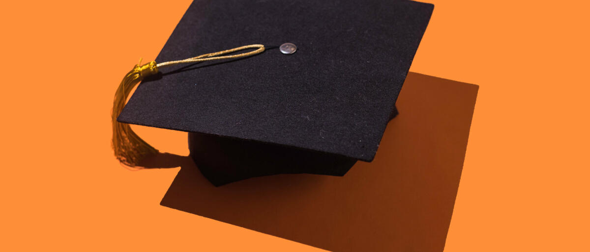Schwarze Graduierungskappe mit goldener Quaste mit Schlagschatten auf orangem Hintergrund. © DBenitostock / Getty Images
