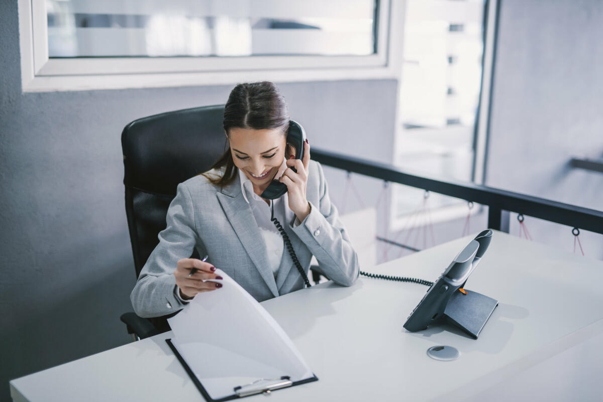 Eine Assistentin plant ein Geschäftstreffen am Telefon in einer Unternehmensfirma.