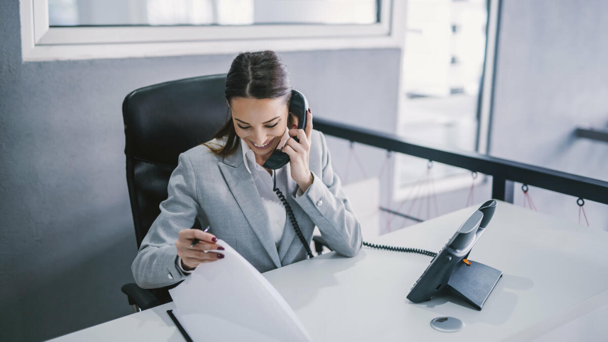 Eine Assistentin plant ein Geschäftstreffen am Telefon in einer Unternehmensfirma.