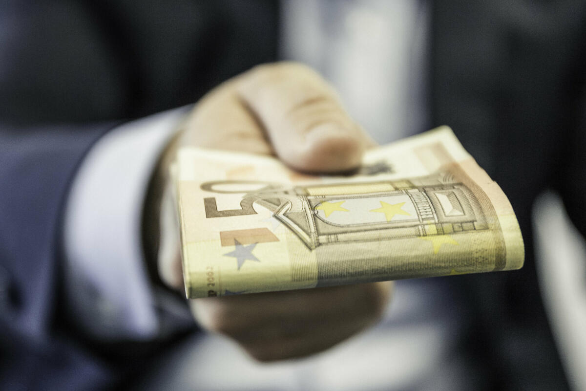 Nahaufnahme eines Geschäftsmannes, der gefaltete Fünfzig-Euro-Noten in der Hand hält © Manuel Sulzer / Getty Images
