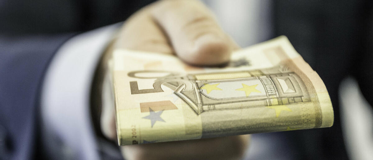 Nahaufnahme eines Geschäftsmannes, der gefaltete Fünfzig-Euro-Noten in der Hand hält © Manuel Sulzer / Getty Images