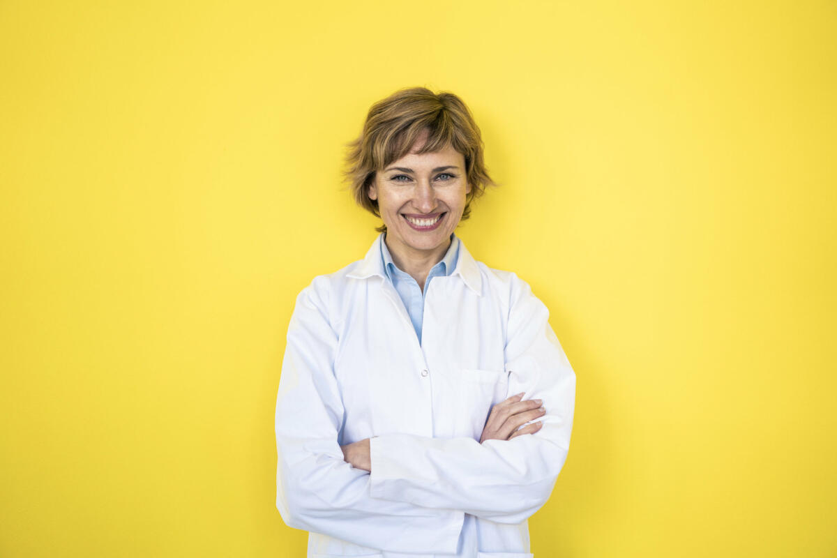 Eine junge Laborantin steht freudig lächelnd vor einem gelben Hintergrund © Westend61 / Getty Imaged