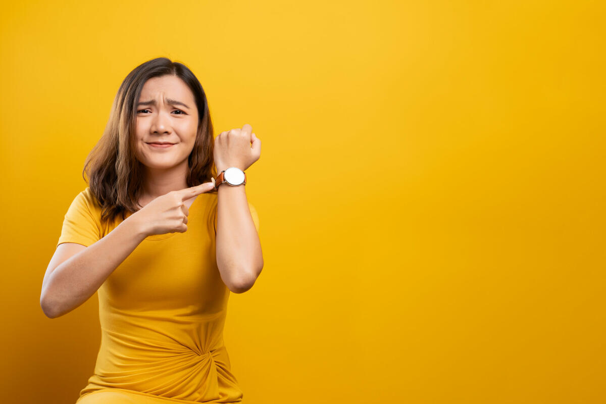 Schockierte Frau hält Hand mit Handgelenksuhr auf gelbem Hintergrund isoliert © champja / Getty Images