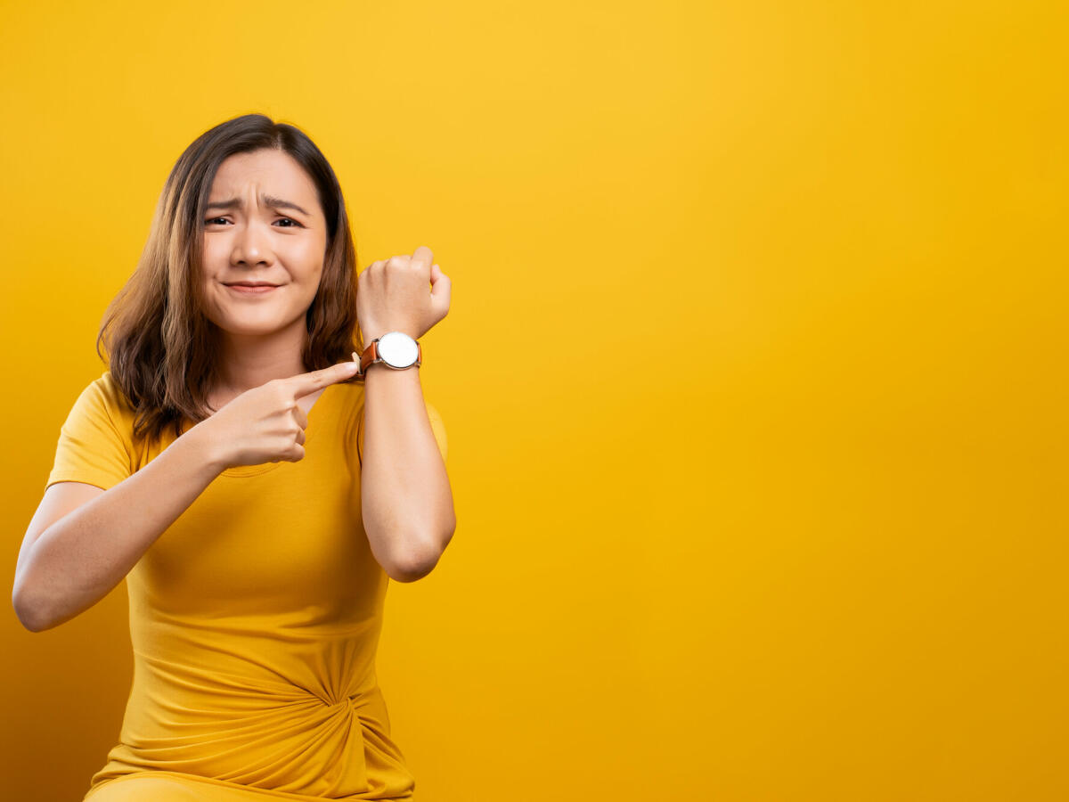 Schockierte Frau hält Hand mit Handgelenksuhr auf gelbem Hintergrund isoliert © champja / Getty Images