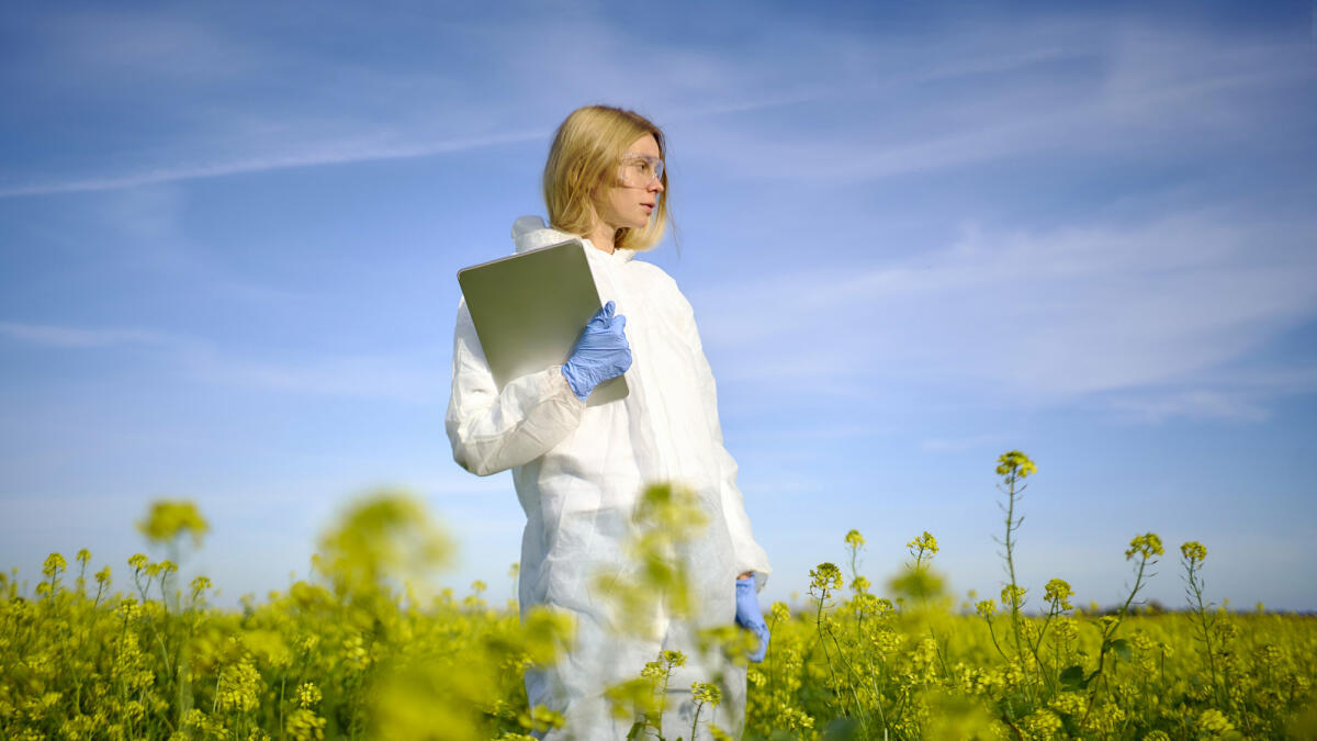 Eine junge Wissenschaftlerin steht im Schutzanzug mit einem Laptop in der Hand auf einem Feld. © Andriy Onufriyenko / Getty Images