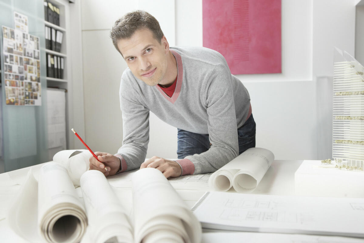 Junger Bauzeichner arbeitet an seinem Schreibtisch an einem Entwurf © Tom Merton / Getty Images