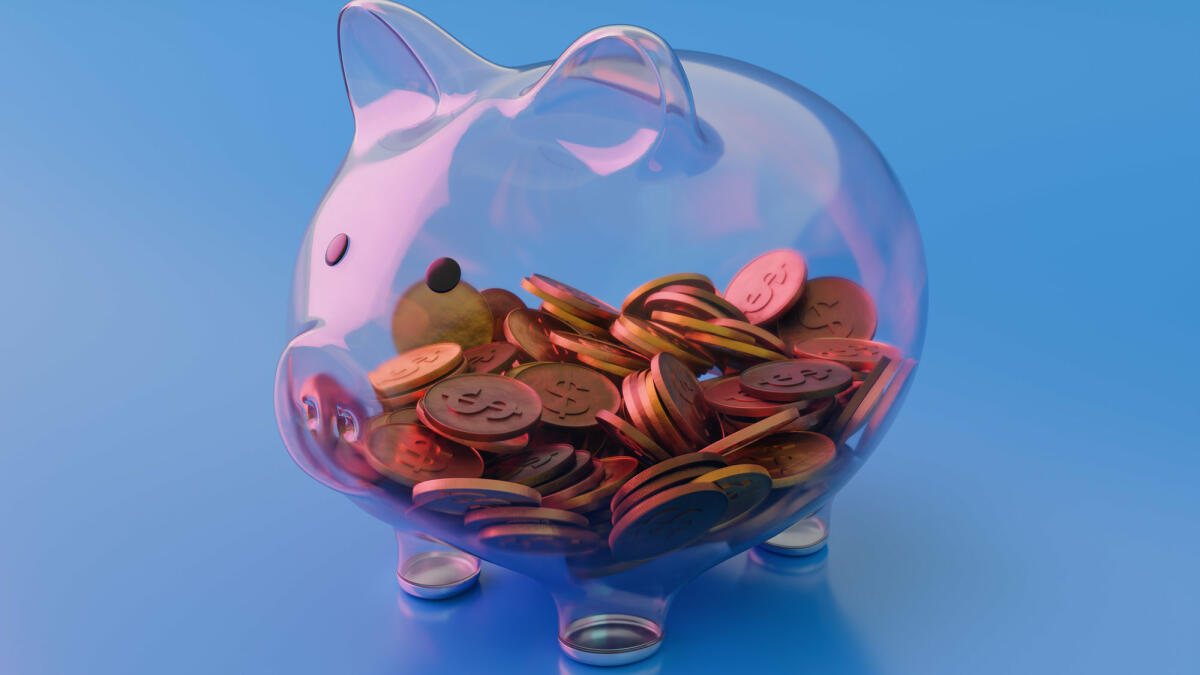 Sehen Sie durch transparentes Glas Sparschwein mit Münzen auf blauem Hintergrund © Constantine Johnny / Getty Images