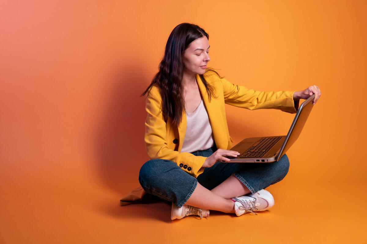 Junge Frau in Gelb macht Geschäfte an einem Laptop, ein Freiberufler oder ein Student arbeitet aus der Ferne. © Aleksandr Koltyrin / Getty Images