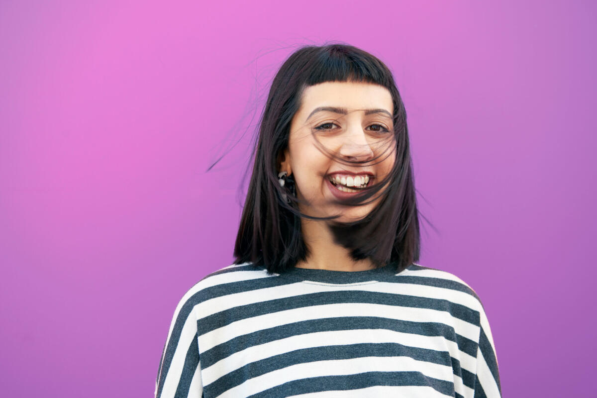 young woman in front of studio wall, laughing, hair swept into her face