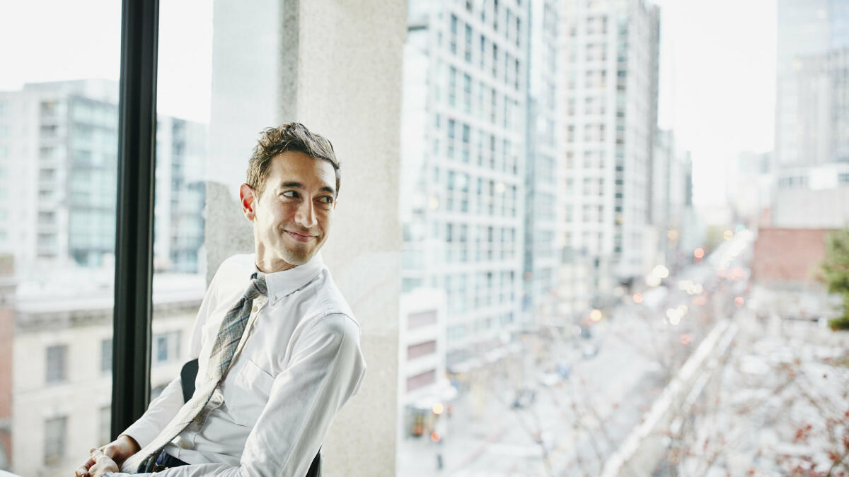 Geschäftsmann im Büro sitzend mit Blick auf die Stadt © Thomas Barwick / Getty Images