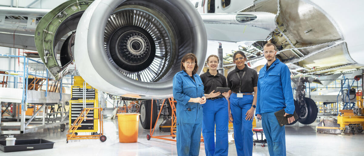 Eine Gruppe von Flugzeugingenieuren, in blauen Anzügen in einer Flugzeugwartungsfabrik. © Monty Rakusen/ Getty Images