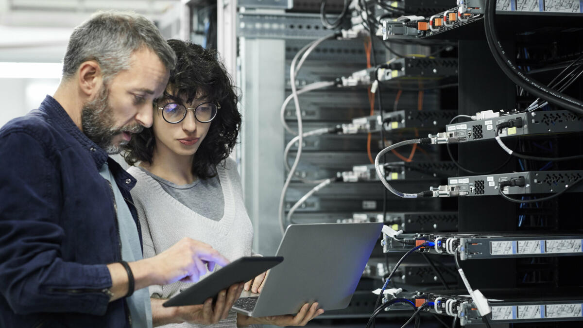 Männlicher Techniker zeigt einer Kollegin ein digitales Tablet. Ingenieur arbeitet mit einem Kollegen am Arbeitsplatz. Sie sind im Serverraum. © Getty Images/ 	Morsa Images