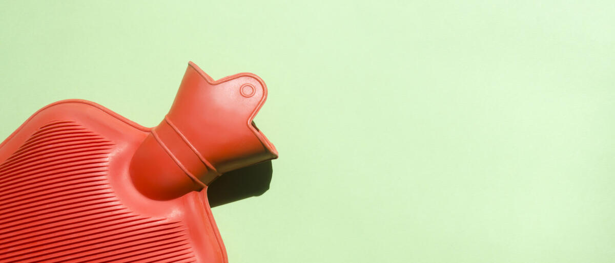 Rote Wärmflasche auf grünem Hintergrund. © Elizabeth Fernandez/ Getty Images