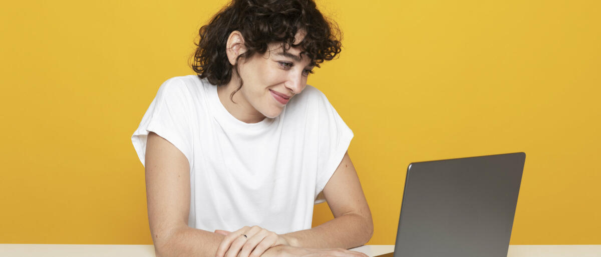 Lächelnde Frau bei der Arbeit am Laptop auf gelbem Hintergrund © Westend61 / Getty Images