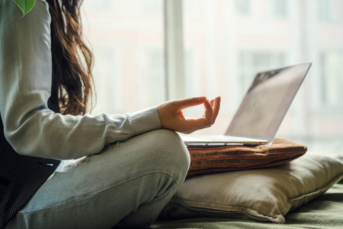 Frau sitzt meditierend vor Laptop. © Fiordaliso / Getty Images