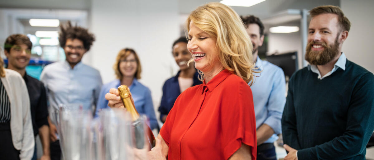 Frau öffnet Sektflasche in Büro © Luis Alvarez / Getty Images
