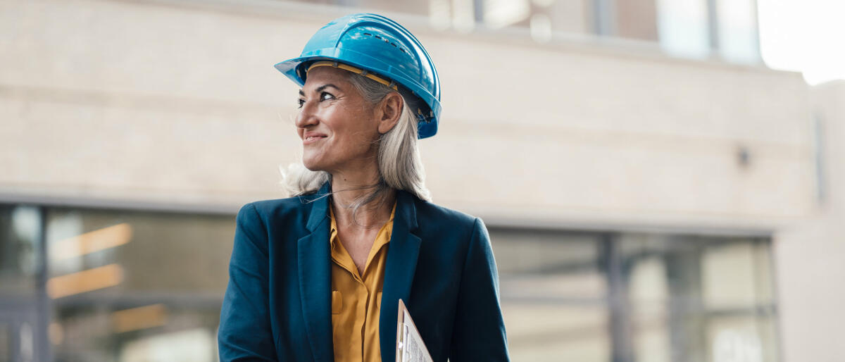 Reife Ingenieurin steht auf einer Baustelle und lächelt © Westend61 / Getty Images