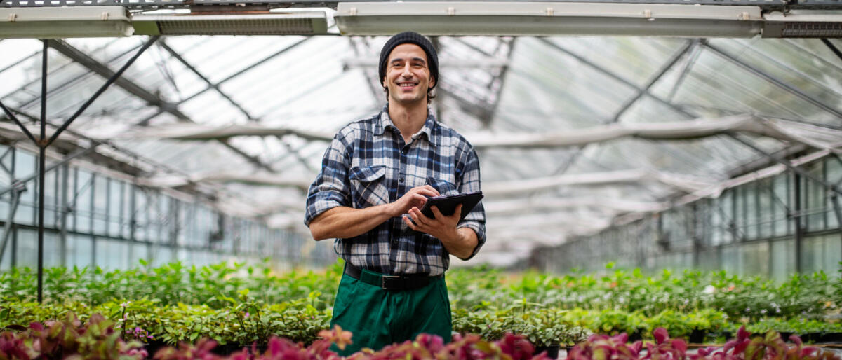 Porträt eines jungen erwachsenen männlichen Gartenarbeiters, der ein digitales Tablet im Gewächshaus benutzt. Mann mit einem Tablet-Computer für Informationen ü © Luis Alvarez/ Getty Images