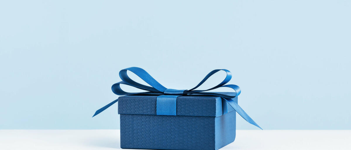 Eine Geschenkbox mit blauer Schleife auf hellblauem Monochrom © Tatiana Sviridova / Getty Images