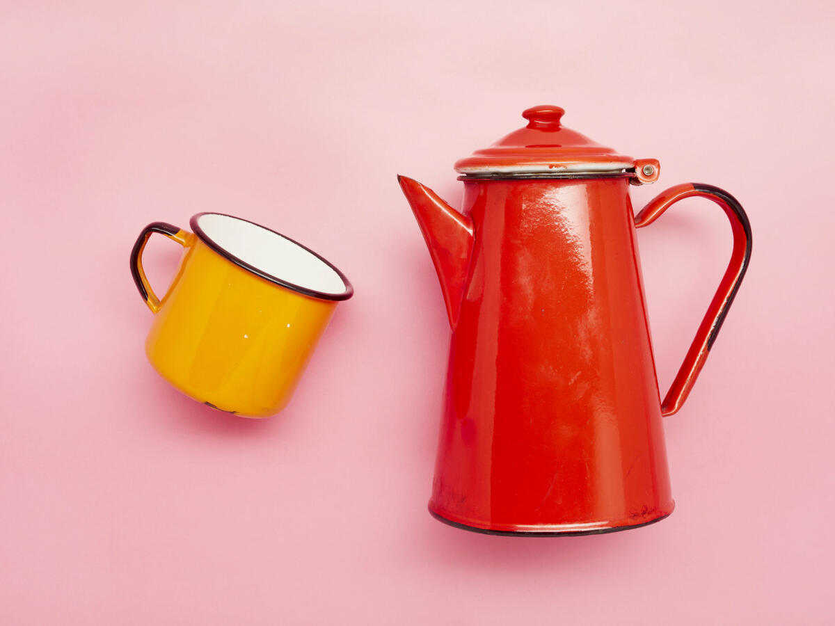 Stilleben einer Emaille-Tasse und einer roten Kaffeekanne auf rosa Hintergrund © the_burtons / Getty Images