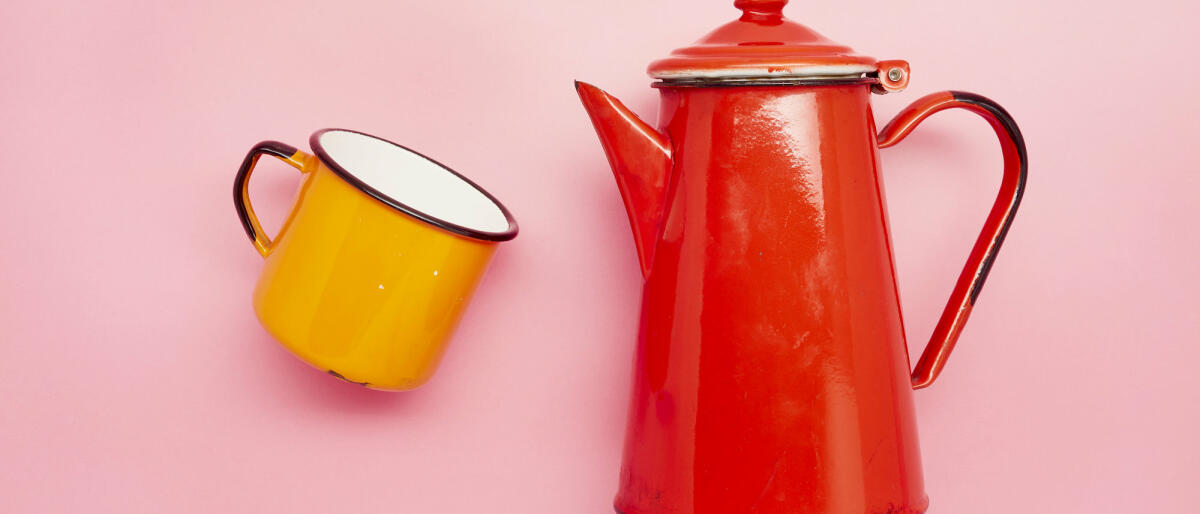 Stilleben einer Emaille-Tasse und einer roten Kaffeekanne auf rosa Hintergrund © the_burtons / Getty Images