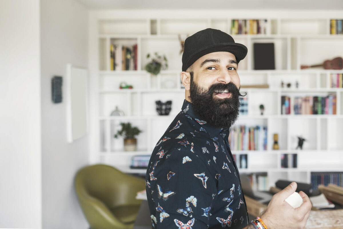 Ein moderner Mann mit langem Bart und Cap guckt von der Seite freundlich ins Bild © Maskot / Getty Images