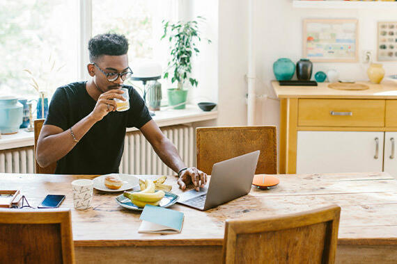 Mann mit Glas in der Hand vor dem Laptop © Maskot / Getty Images