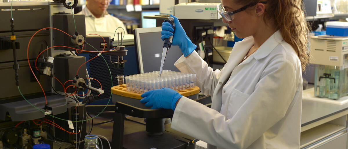 Eine junge Bioechemikerin steht im Labor und führt ein Experiment mit einer Pipette durch © Peter Dazeley / Getty Images