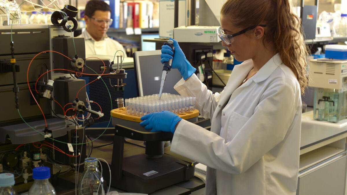 Eine junge Bioechemikerin steht im Labor und führt ein Experiment mit einer Pipette durch © Peter Dazeley / Getty Images