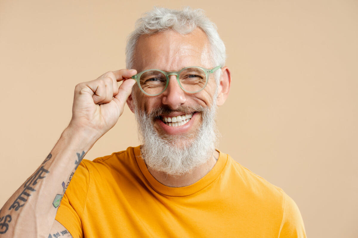 Erfolgreicher reifer Mann, der eine stilvolle Brille und ein gelbes T-Shirt trägt, isoliert auf beigefarbenem Hintergrund © Mariia Vitkovska / Getty Images