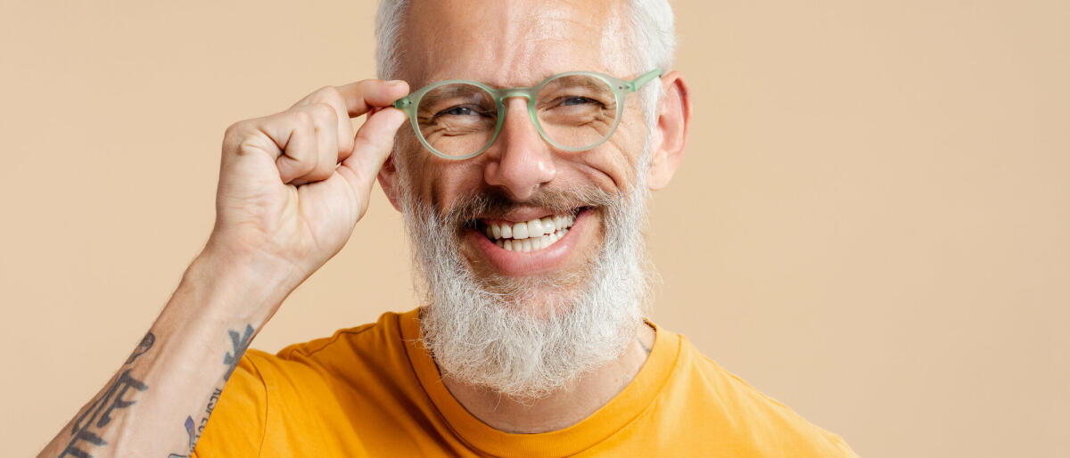 Erfolgreicher reifer Mann, der eine stilvolle Brille und ein gelbes T-Shirt trägt, isoliert auf beigefarbenem Hintergrund © Mariia Vitkovska / Getty Images