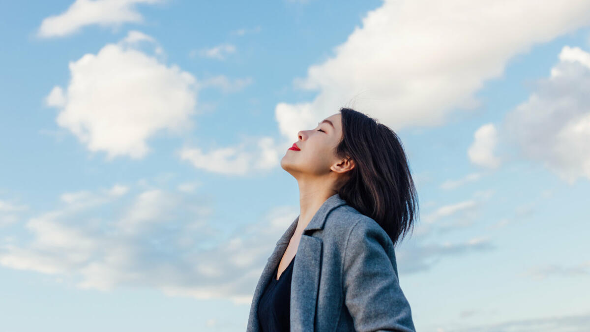 Eine Frau atmet tief ein vor blauem Himmel © Oscar Wong / Getty Images