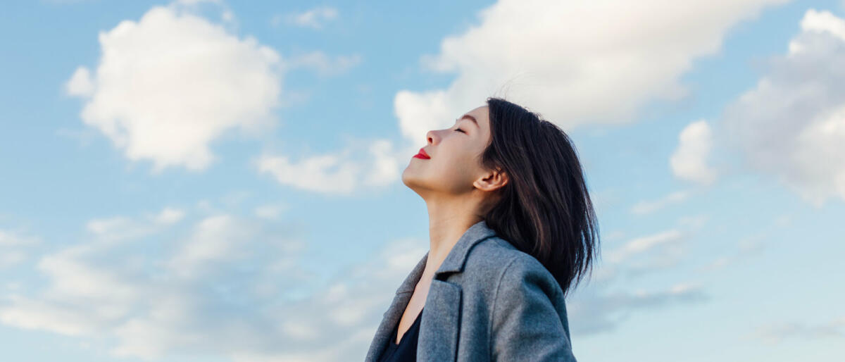 Eine Frau atmet tief ein vor blauem Himmel © Oscar Wong / Getty Images