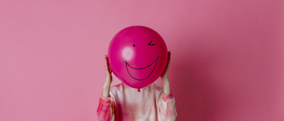 Frau hält einen rosa Ballon mit einem Lächeln auf dem Ballon vor ihrem Gesicht © SolStock / Getty Images