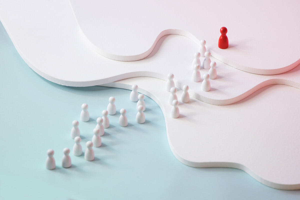 One red figurine leading a row of white figurine on coloured background. © twomeows / getty images