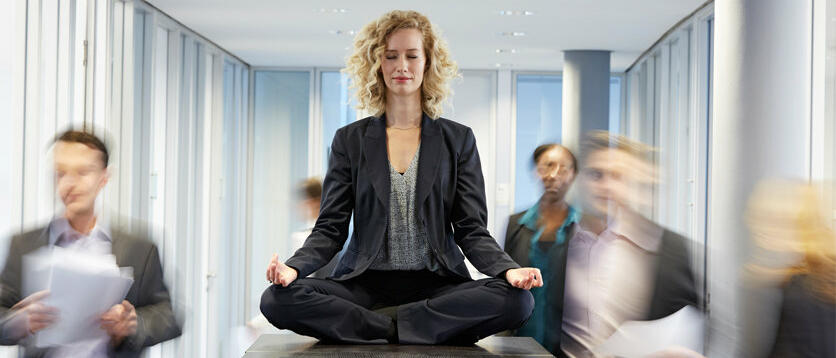 Eine Frau sitzt in Meditations-Position auf deinem Tisch im Büro © Westend61 / Getty Images