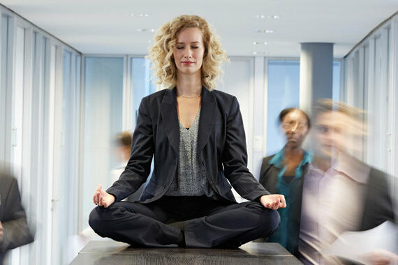Eine Frau sitzt in Meditations-Position auf deinem Tisch im Büro © Westend61 / Getty Images